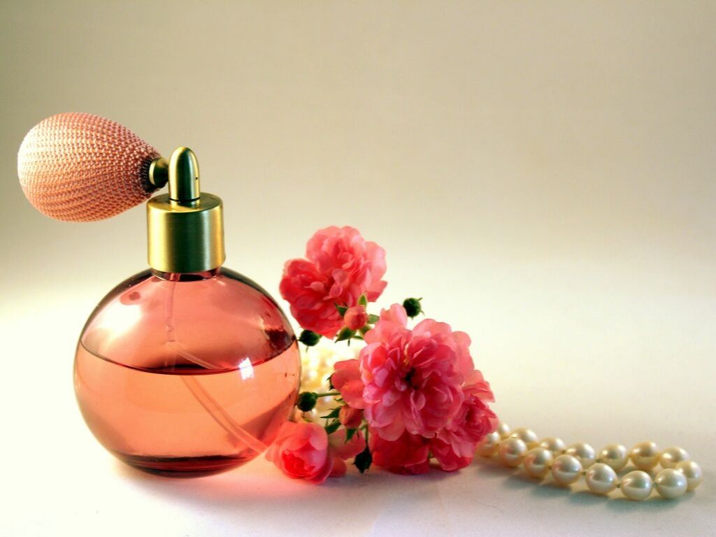 Un flacon de parfum avec des fleurs et un collier de perles