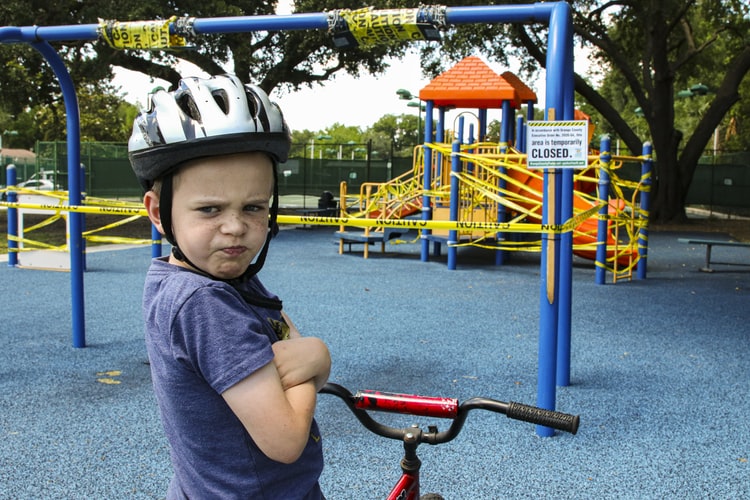 Jeune garçon qui boude sur son vélo, dans une aire de jeux pour enfants. 