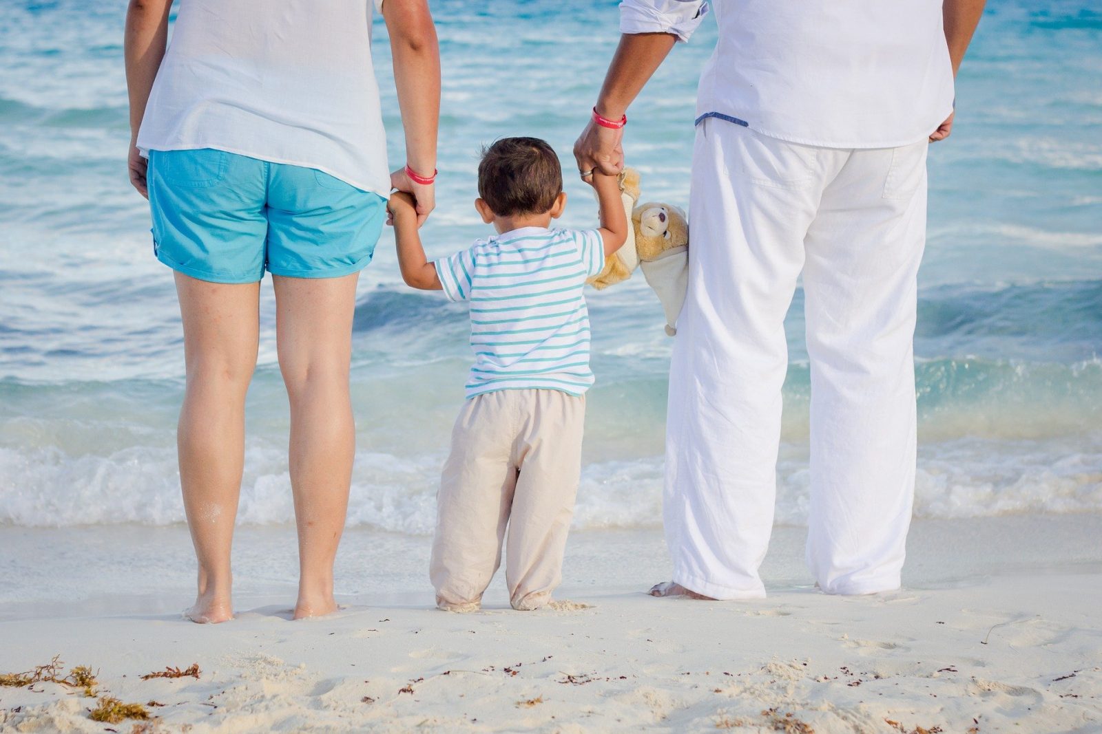 Un enfant tenant ses parents par la main au bord de la mer sur la plage.
