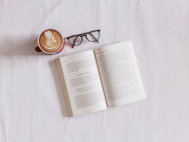Livre ouvert sur une table avec une tasse de café et une paire de lunettes