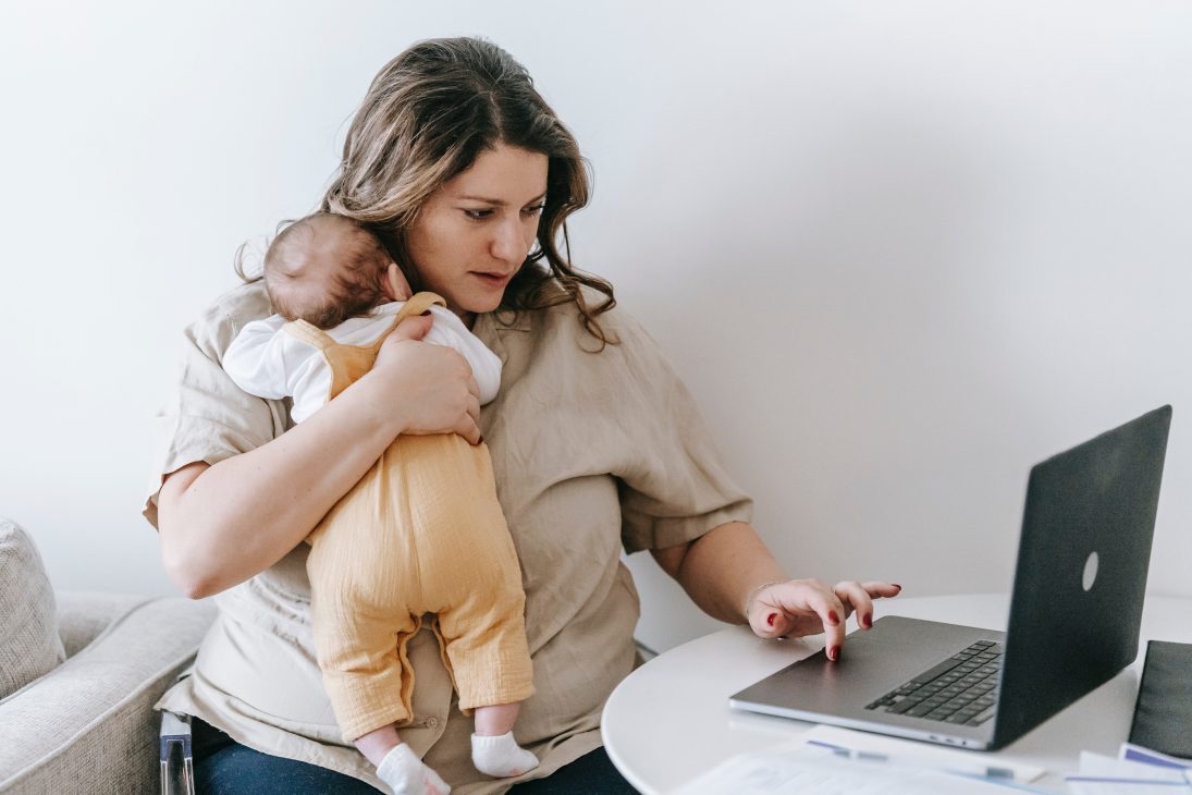 Maman débordée qui travaille sur son ordinateur avec son bébé dans les bras