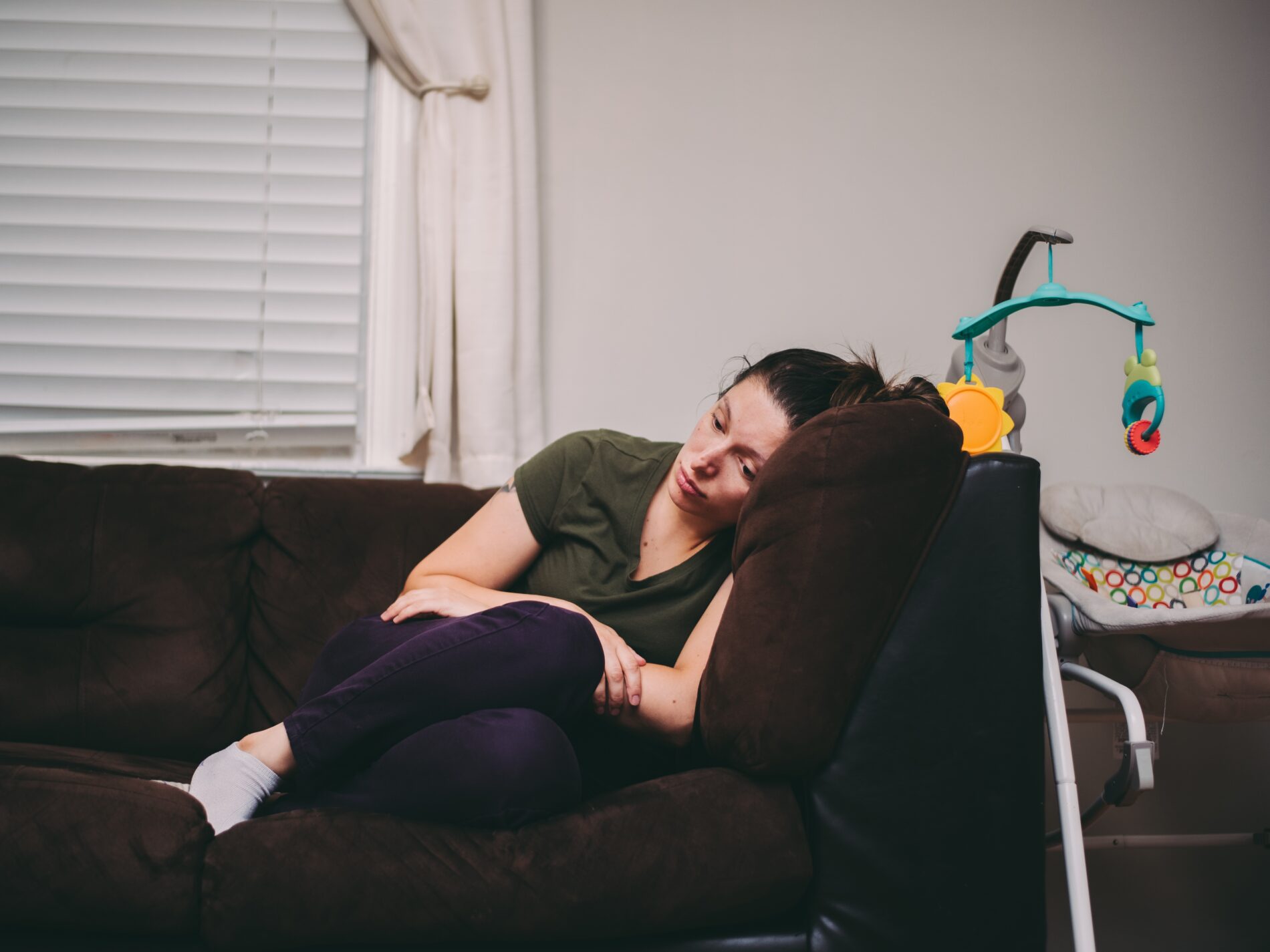Femme présentant des symptômes de dépression post-partum, assise en boule sur son canapé.